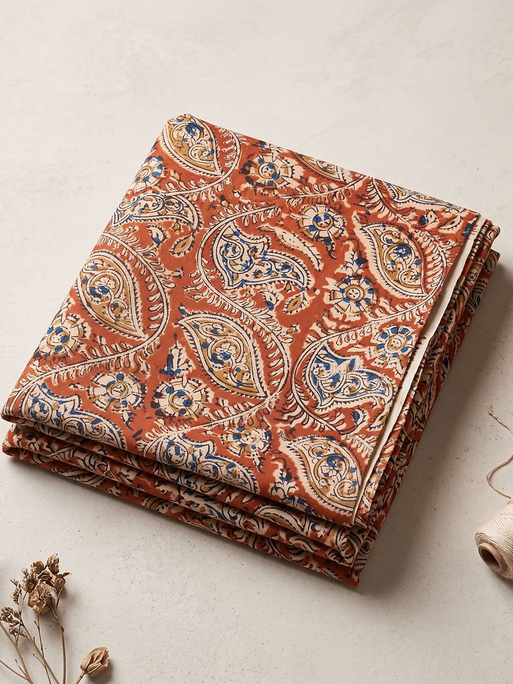 Ambika rust paisley Kalamkari cotton fabric folded flat: large cream paisleys with blue and mustard flowers on a brick-rust ground