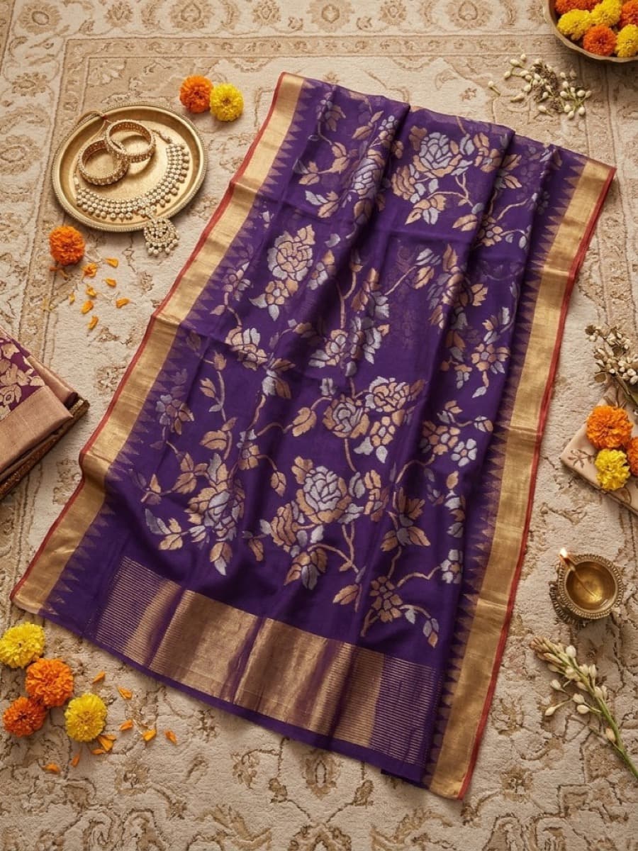 Aparajita purple Jamdani saree flat lay with gold haar, marigolds and a lit diya