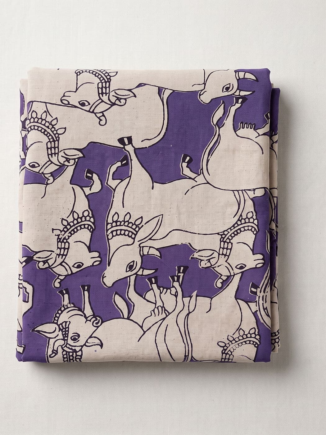 Gomati violet Kalamkari cotton fabric folded flat: cream Nandi cows outlined in black, nose to tail across a violet ground