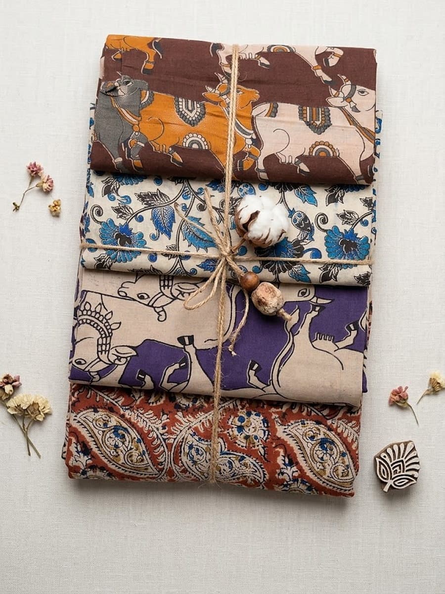 All four Kalamkari cotton pieces folded and tied with twine: brown Nandi dupatta, blue floral dupatta, violet Nandi fabric and rust paisley fabric