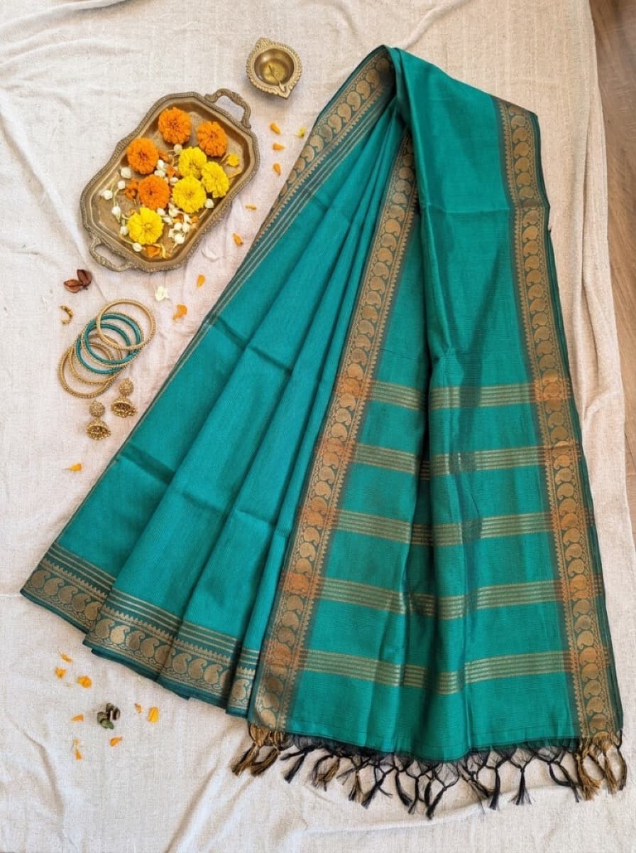 Mayura teal saree flat lay with marigolds and gold jewellery
