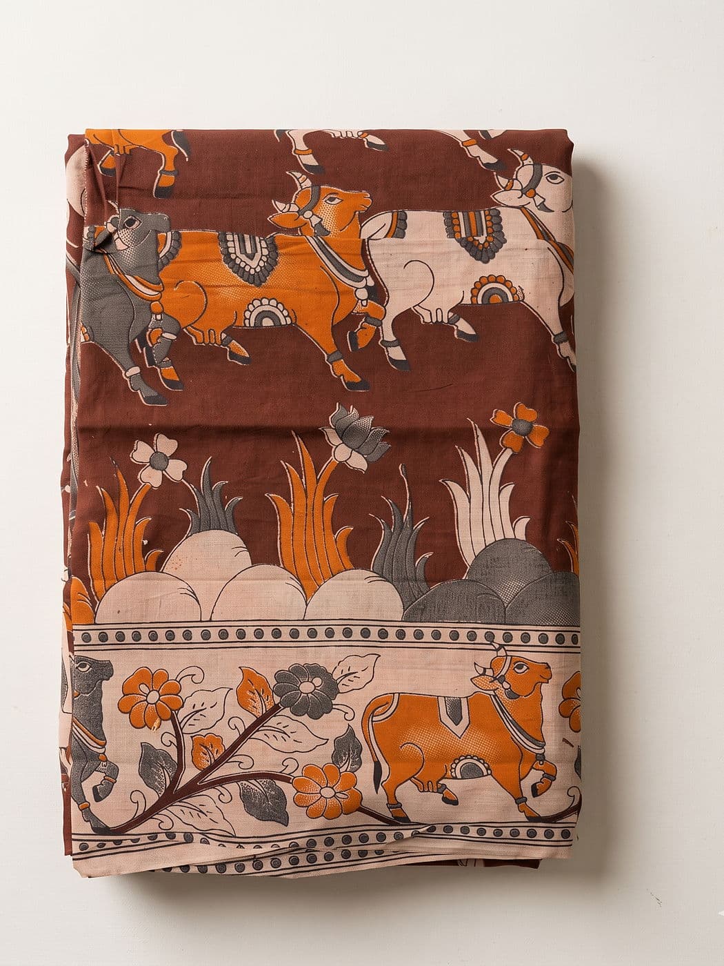 Nandini brown Kalamkari cotton dupatta folded flat: orange, grey and cream Nandi cows above a lotus pond, cream floral border along the edge